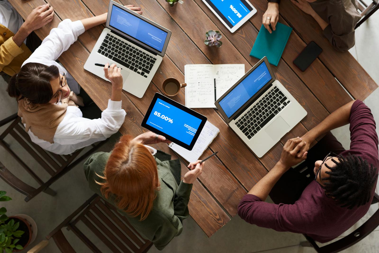 Diverse team discussing business strategies with laptops and tablets at a wooden table, group benefits